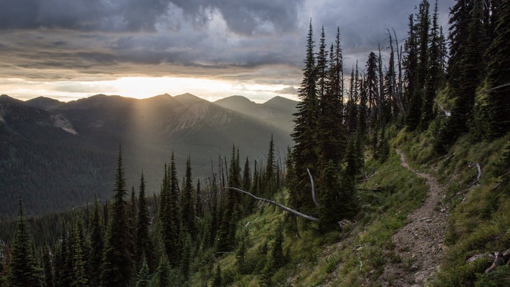 Trail in mountains with sunbeams shining through clouds