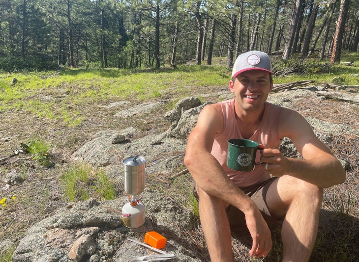 Man sits on ground holding a coffee mug