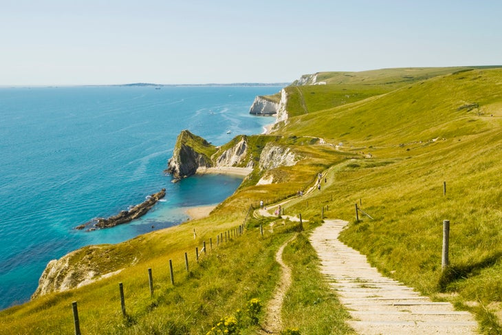 A dirt path alongside cliffs above a turquoise ocean.