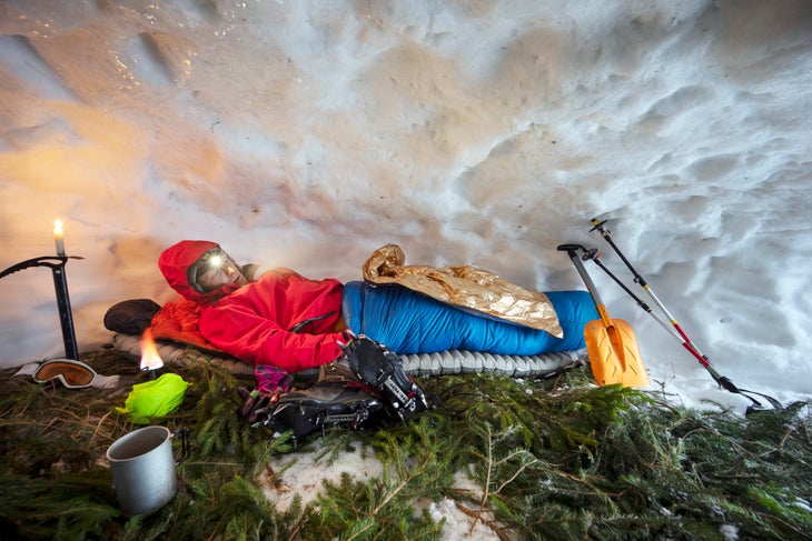 A mountain climber reclines in a sleeping bag inside a snow cave. (Photo: panaramka/Getty)