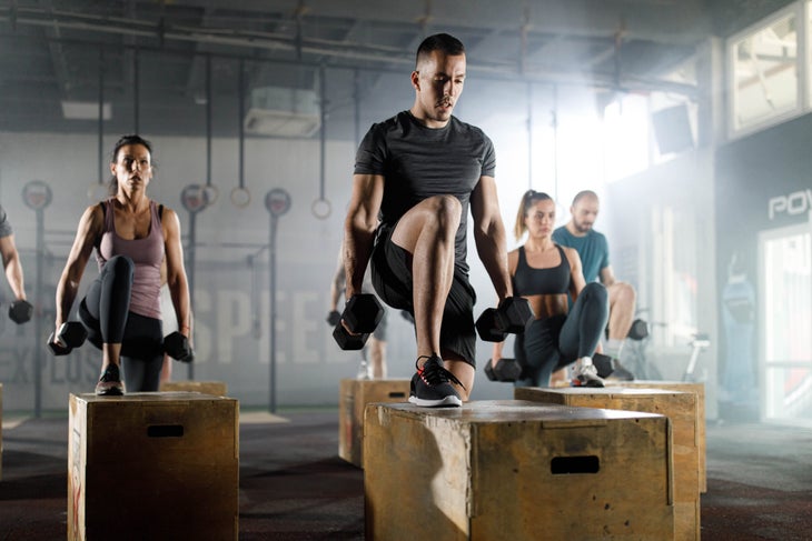 A group of athletic-looking individuals in a gym do step-ups while holding dumbells