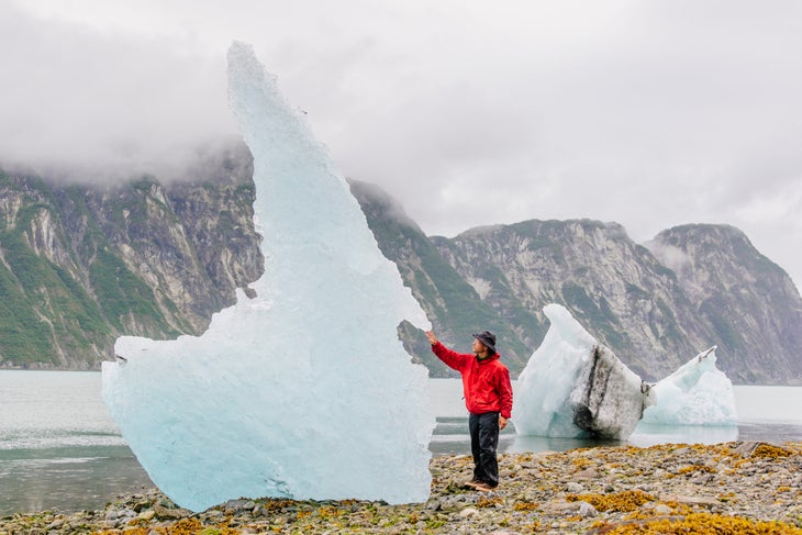 A man in a red jacket stands next to a small iceberg