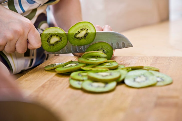 close-up of a hand slicing kiwi to dehydrate