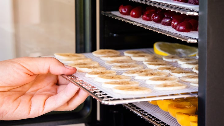 A hand pulling a tray of banana slices out of a dehydrator