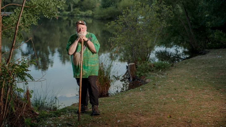 Man leaning on walking stick by lake