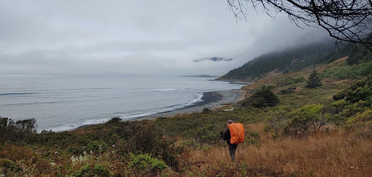 A hiker descends toward the ocean amidst foggy bluffs. 