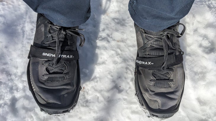 Black hiking shoes with traction devices on them standing on snow