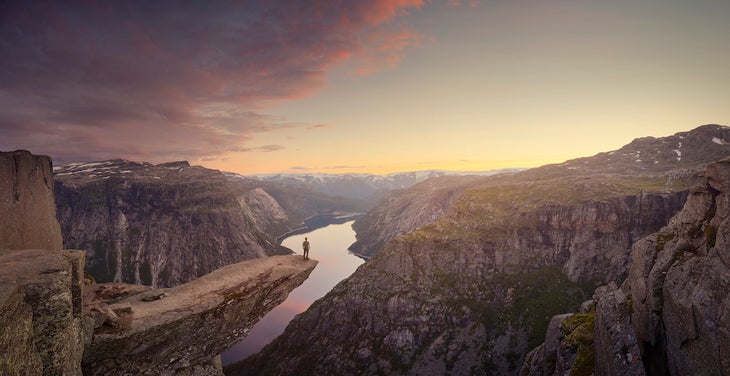 Panoramic of traveller looking out at landscape at sunset, Trolltunga, Norway