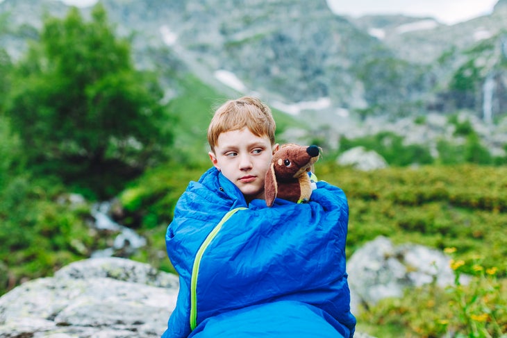 Boy in sleeping bag in the morning while trekking in mountains