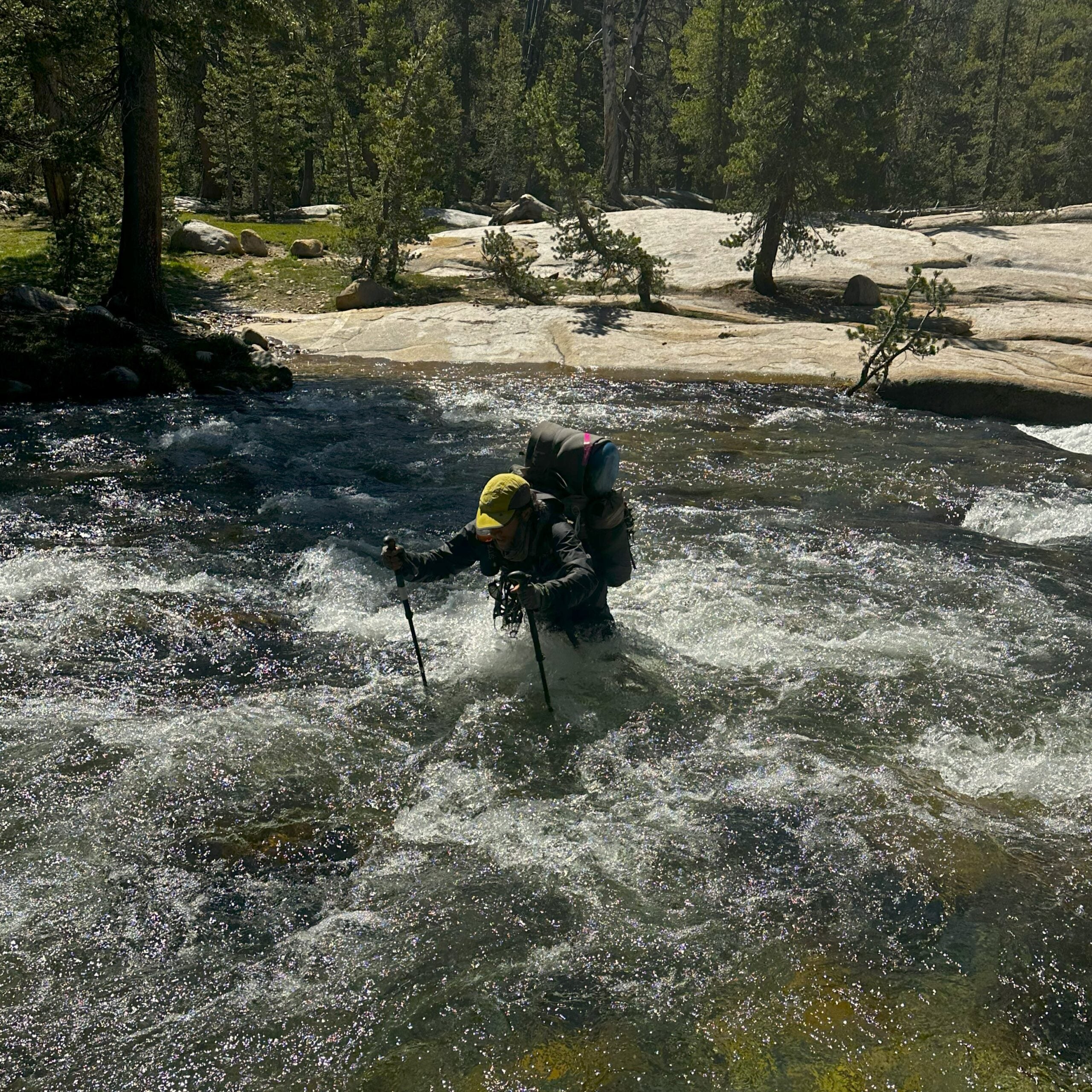 A hiker wading through a waist-deep river