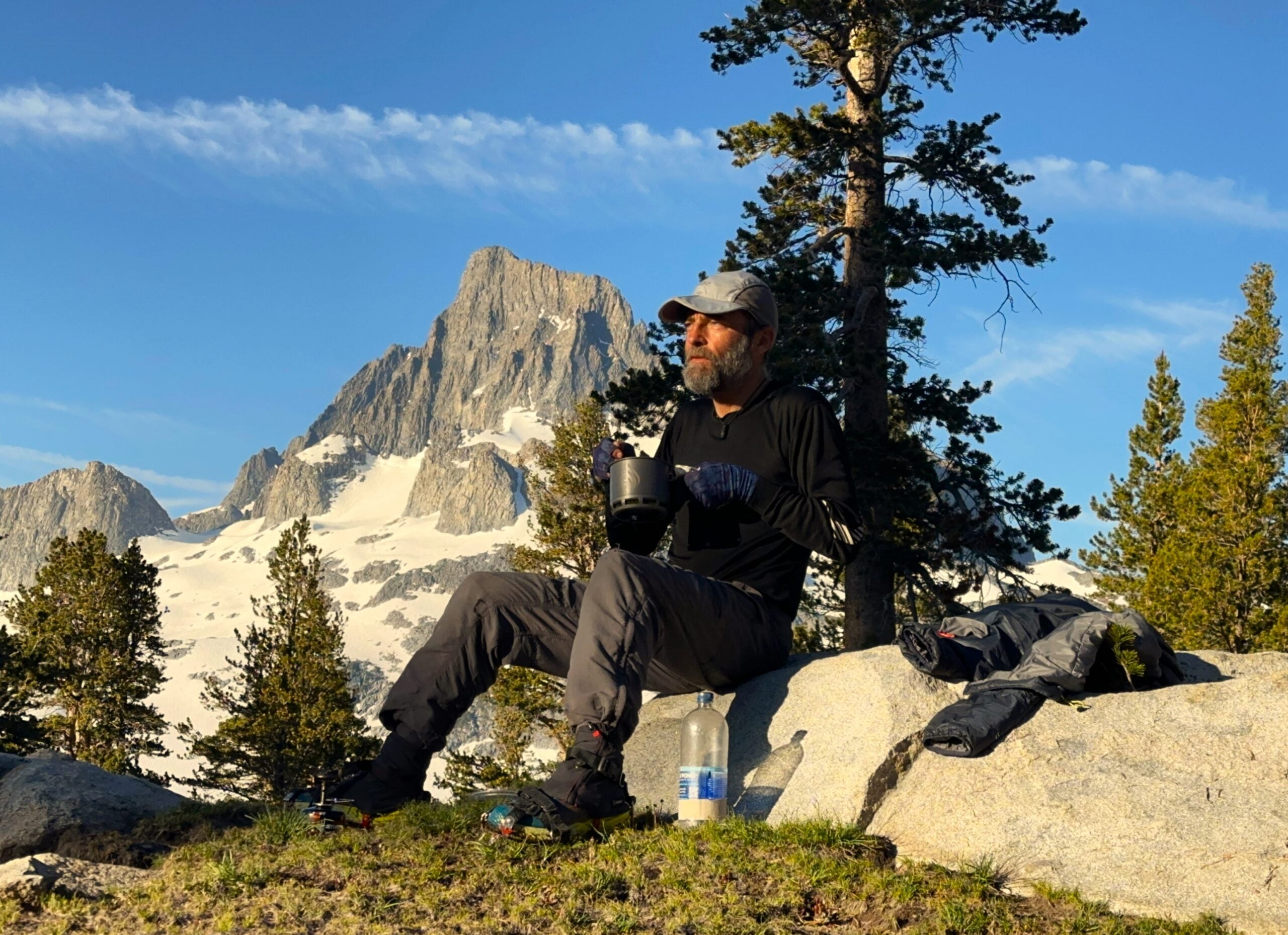 A hiker sits on a rock with granite peaks in the background