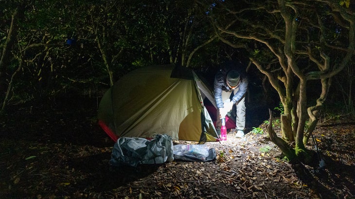 Backpacker wearing headlamp filtering water outside of tent at night
