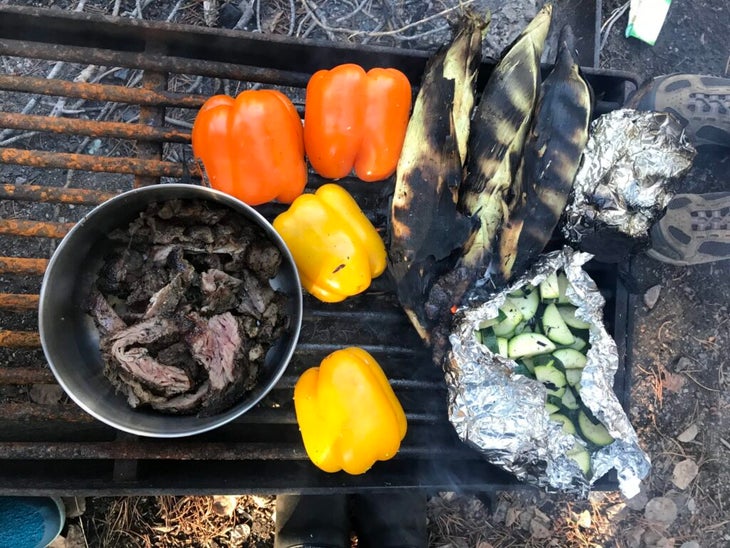 Corn, bell peppers, and steak on a grill over a fire.
