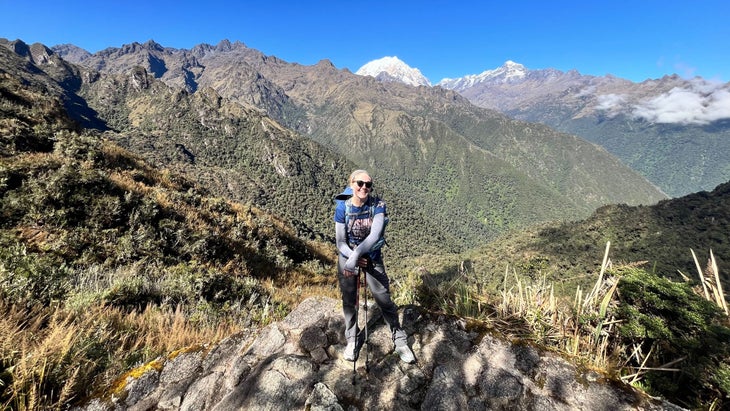 Associate Editor Emma Veidt stands atop a mountain peak on a sunny day.