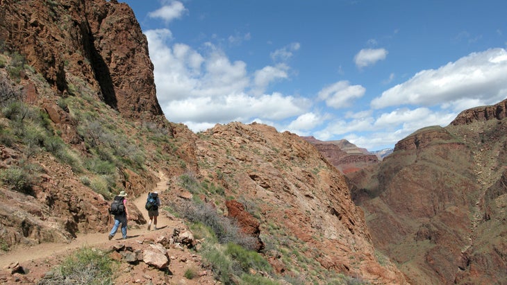 Two hikers in light colored hats and loose clothing hike in hot weather in grand canyon national park.