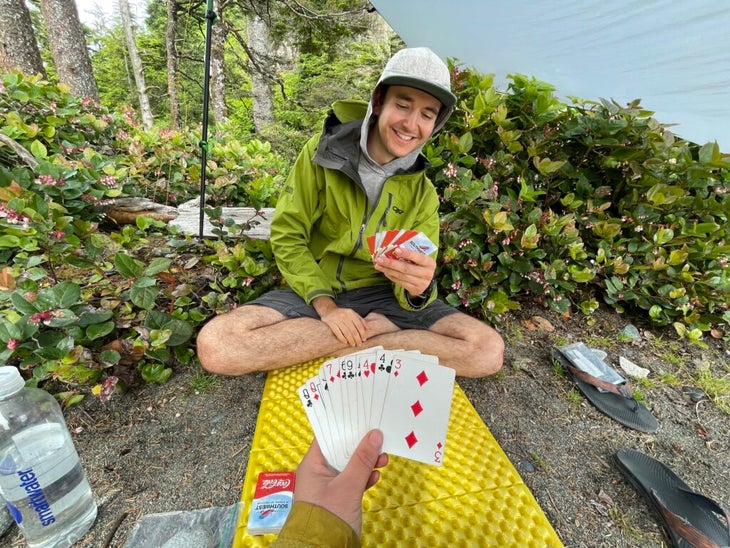 A hiker sits under a tarp playing cards