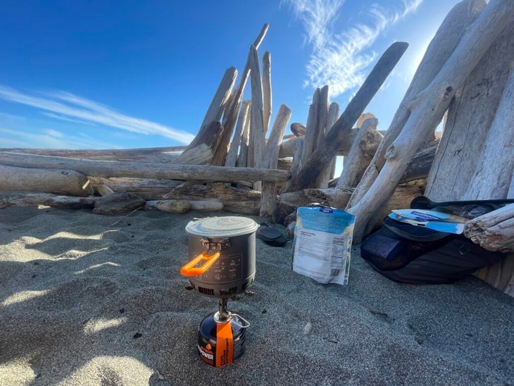 a camp stove in sand in front of driftwood