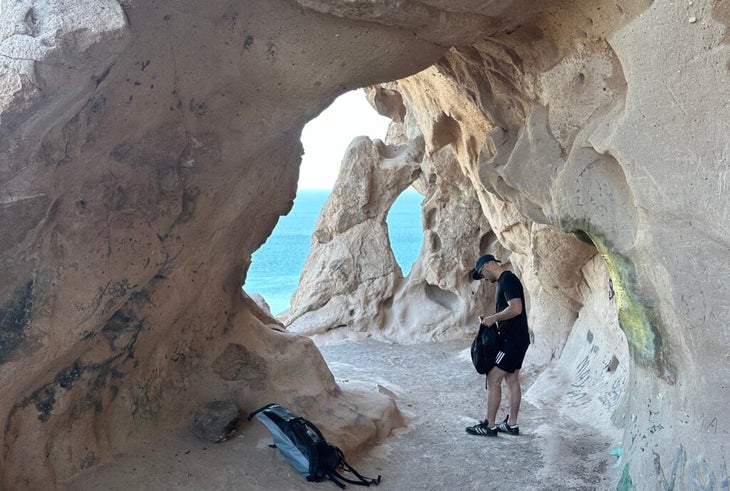 a hiker stands in a wind-carved grotto with ocean views near the coast of Baja Sur California in Mexico.