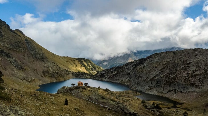 A hut amid grassy hills and a lake in the Pyrenees Mountains in Spain 