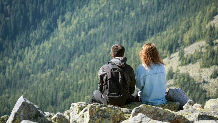 A couple stis close together on a rocky summit in the mountains on a clear day.