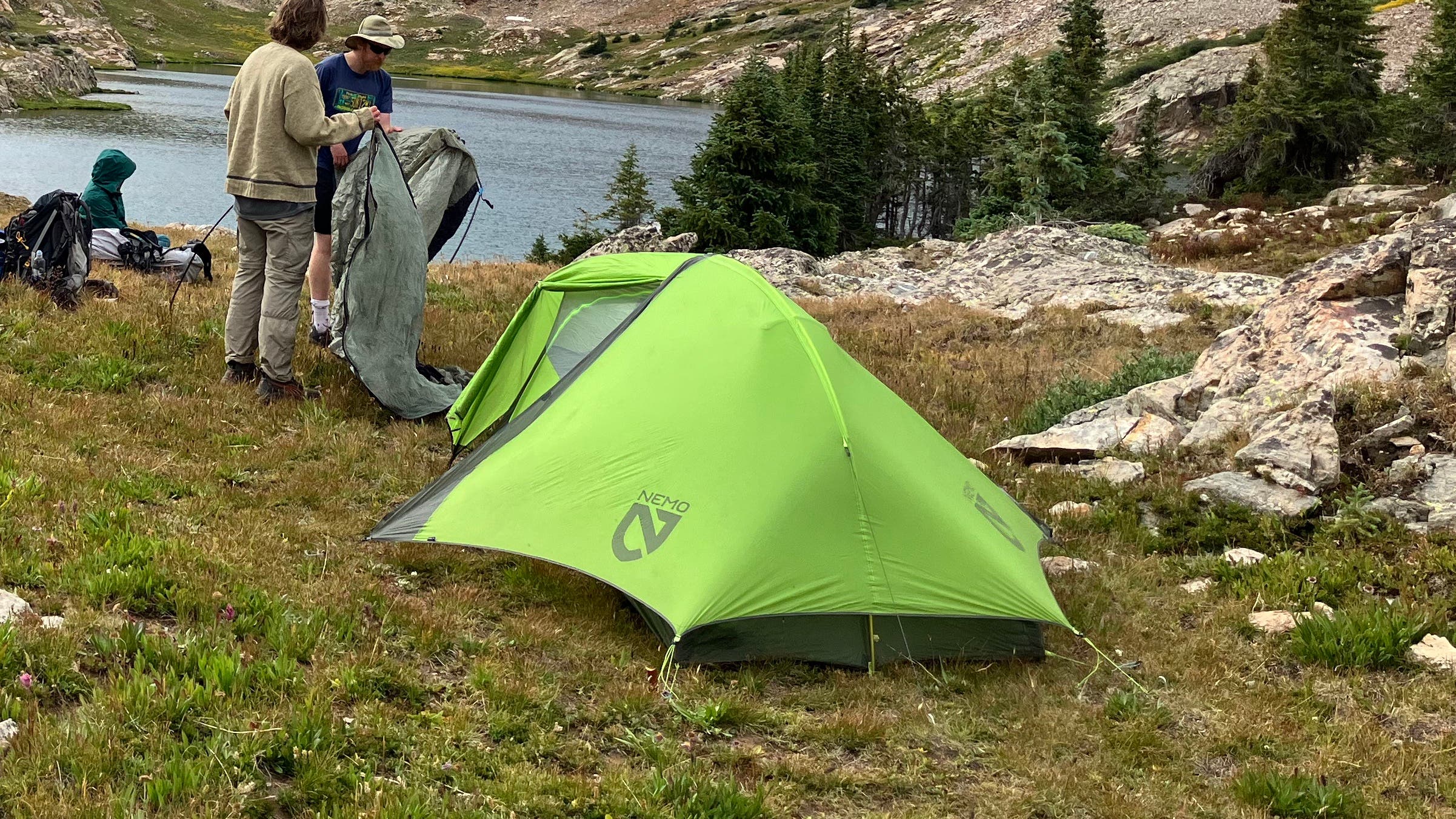 Green tent in an alpine meadow by a lake on a cloudy day