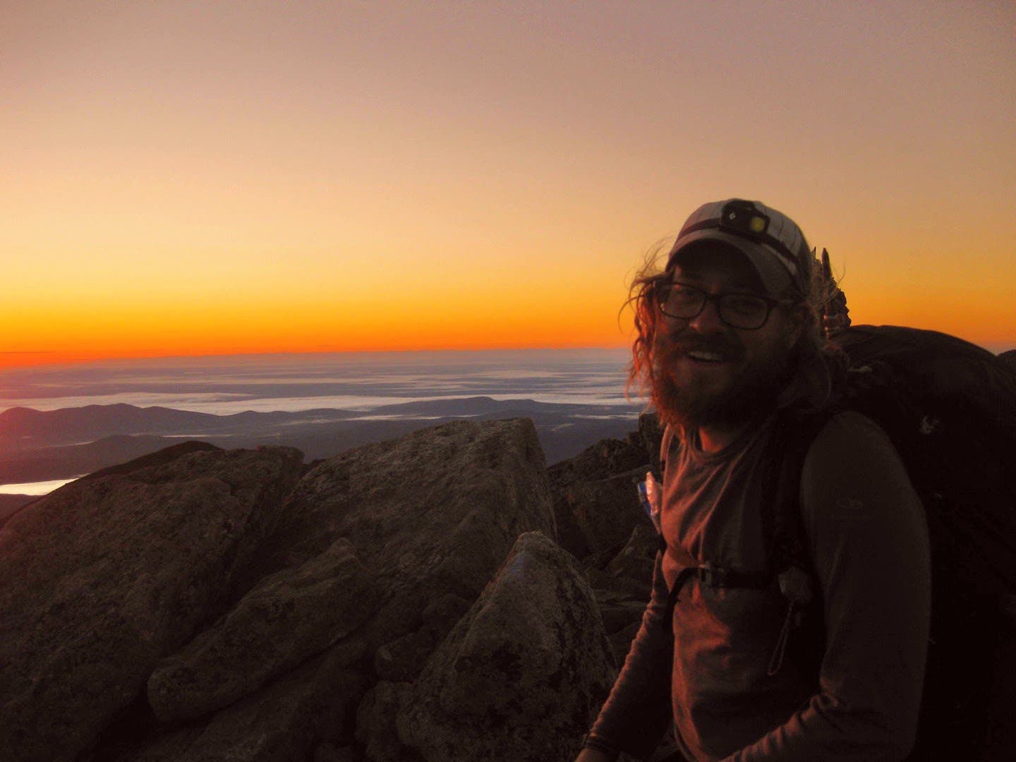 A bearded hiker stands on top of Katahdin