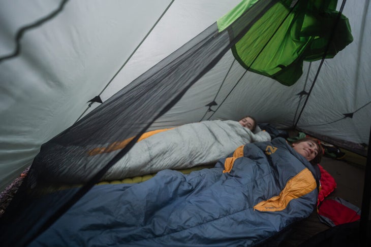 Two campers lying inside sleeping bags in a tent.