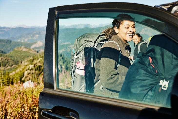 Laughing young woman preparing for backpacking trip hiking without a car