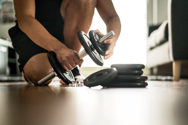 Man adding more weight to adjustable dumbbells at home gym for walkers