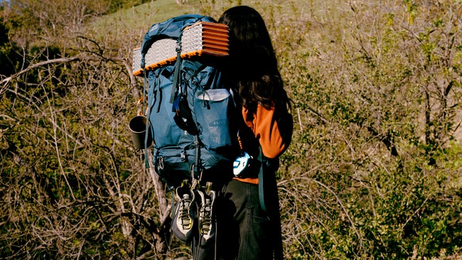 Woman hiker wearing blue backpacking pack with sleeping pad attached