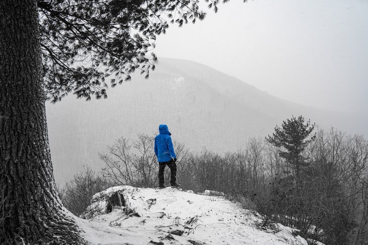 Man in Blue Jacket Standing on Snowy Mountain Overlooking Forest, north country trail