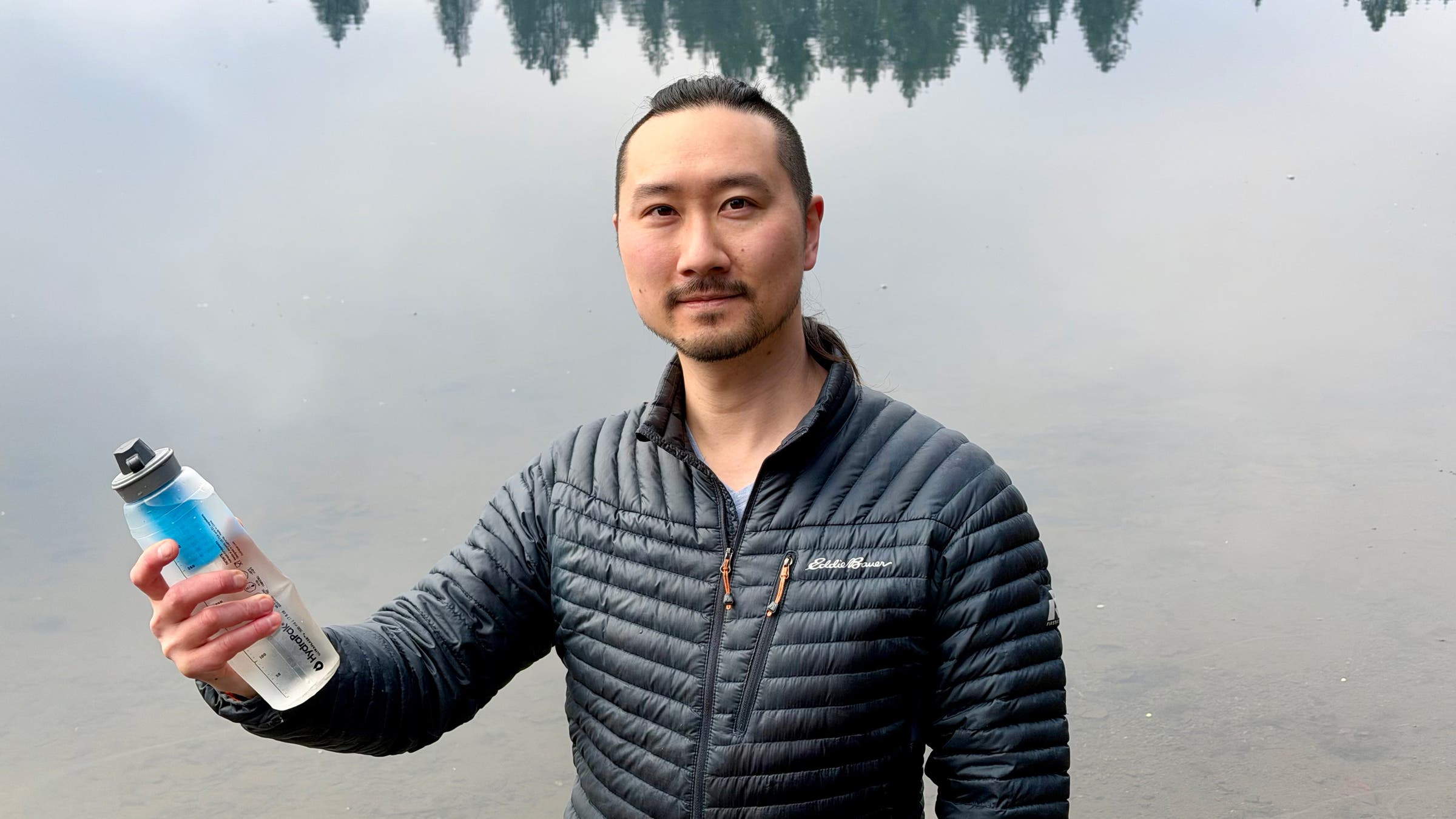 Water filter tester holds HydraPak 42mm water filter in front of lake while backpacking.