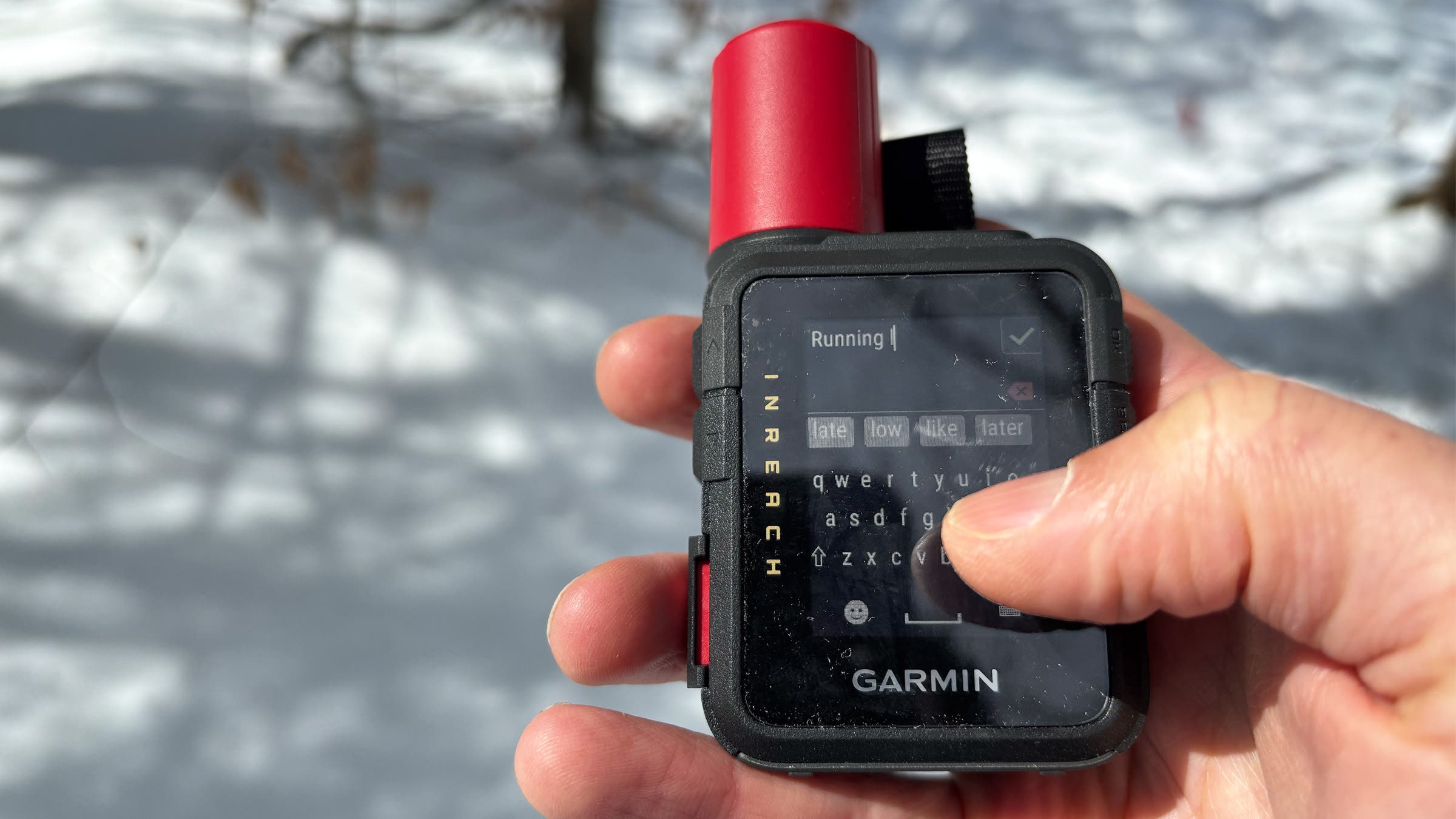 A close-up of a hand using the touchscreen keyboard on the Garmin inReach Mini 3 Plus, highlighting its functionality as the best standalone satellite communicator in a snowy outdoor setting.