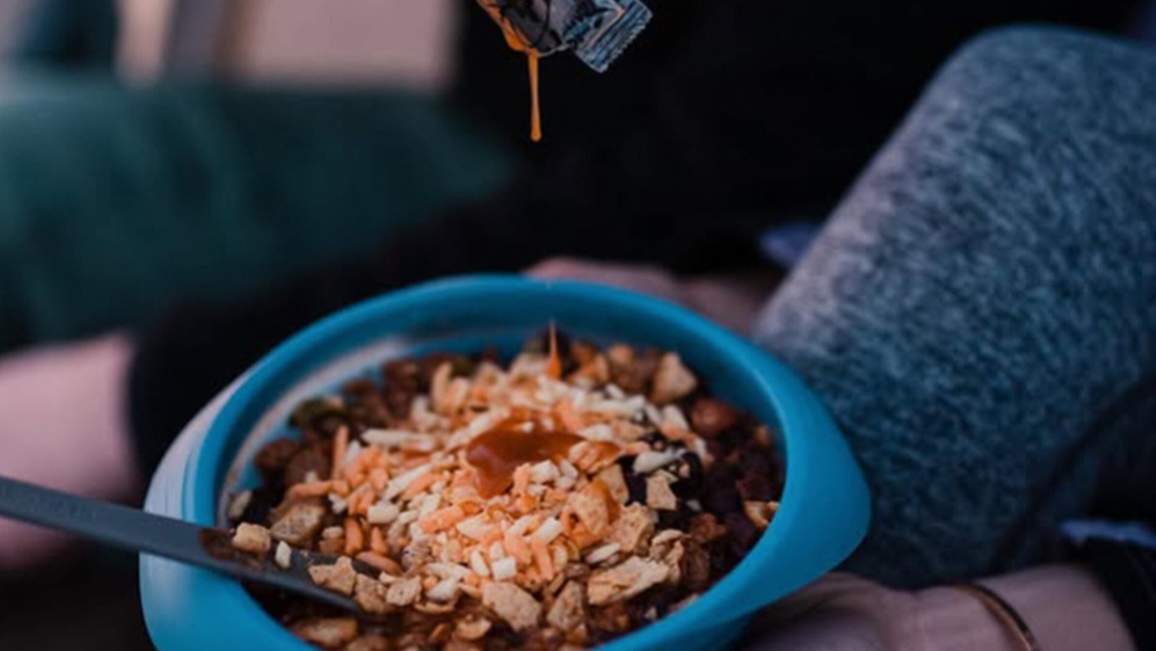 Backpacking meal from Packit Gourmet's chile in a bowl with someone drizzling hot sauce on top