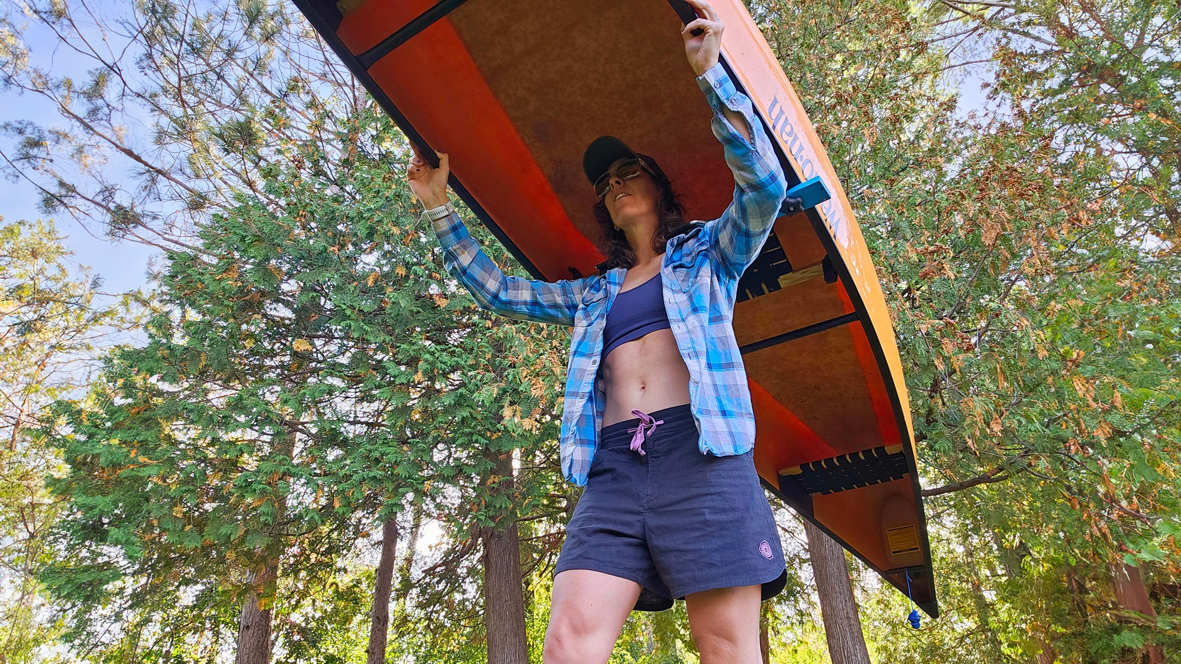 Woman carrying canoe on a portage wearing the Astral Kinisi Hemp Shorts in forest.
