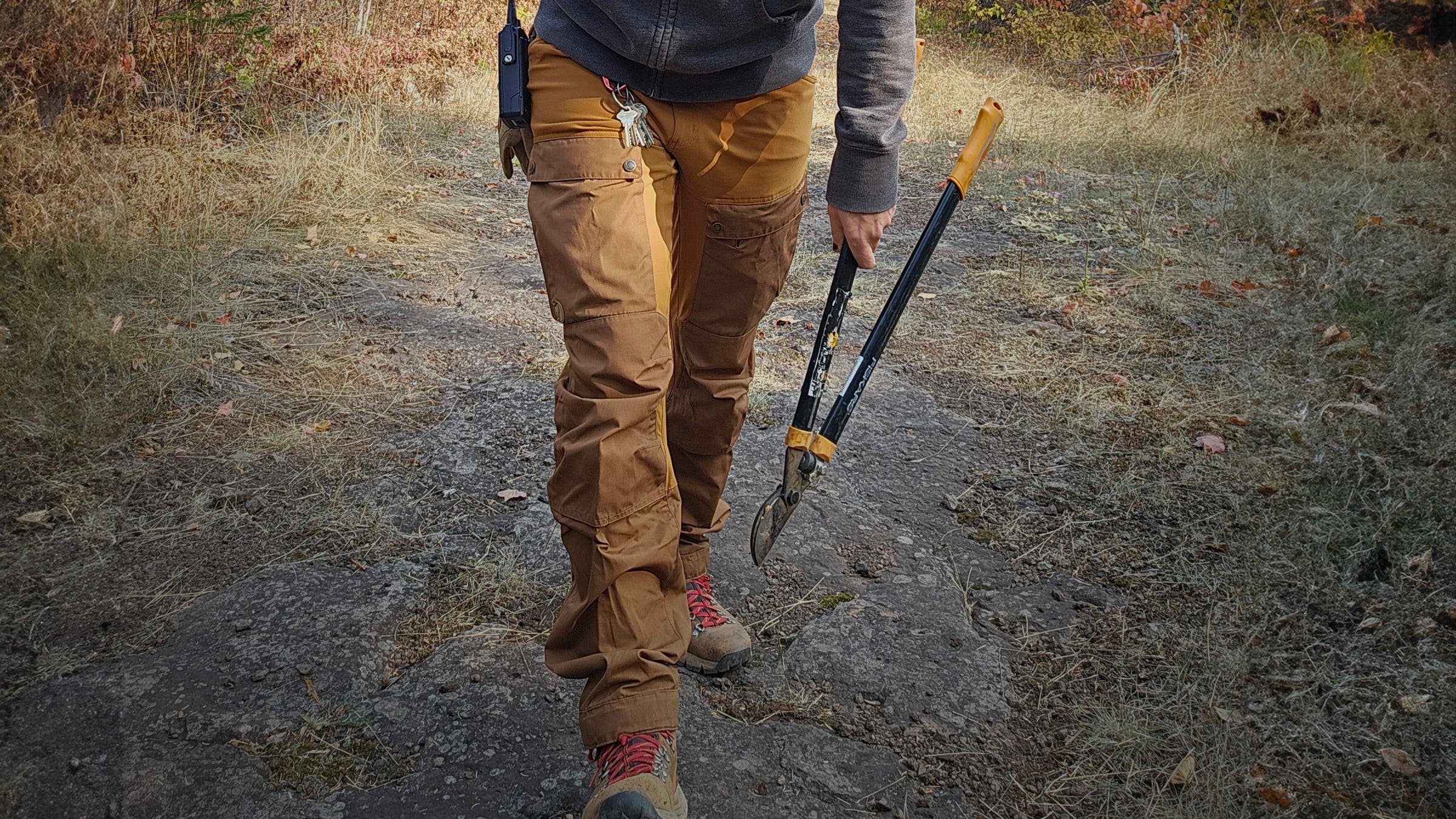 Hiker doing trail work with cutting tools in hand wearing highly durable Fjallraven Keb Trousers with reinforced knees.