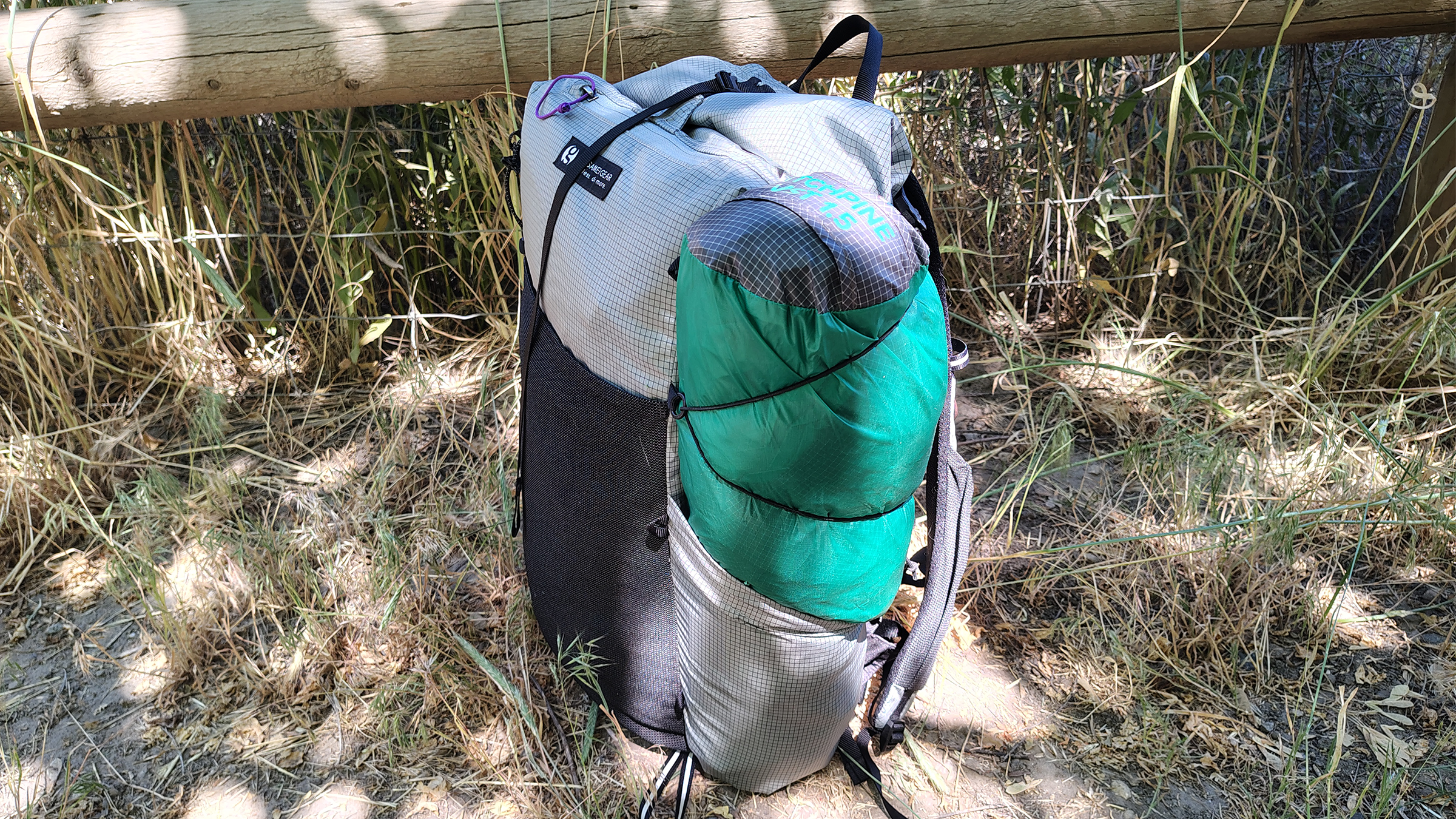 A backpack on the ground with a tent in the side pocket