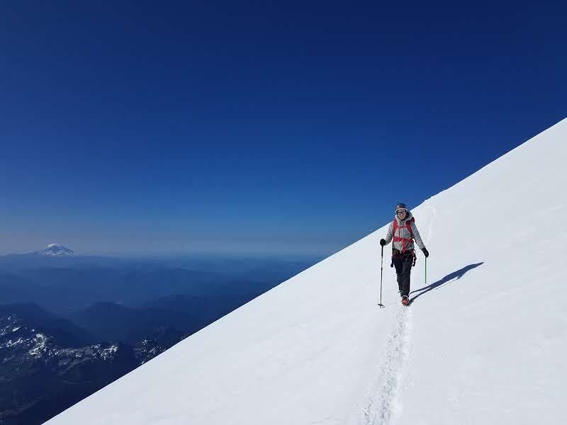 A hiker side-hilling on Mt. Rainier under blue skies